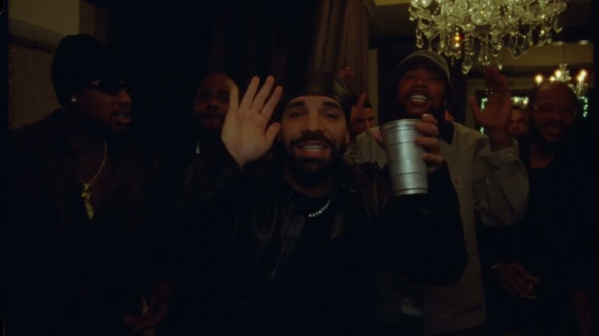 Music video: a man in a black durag raising a silver cup under chandeliers